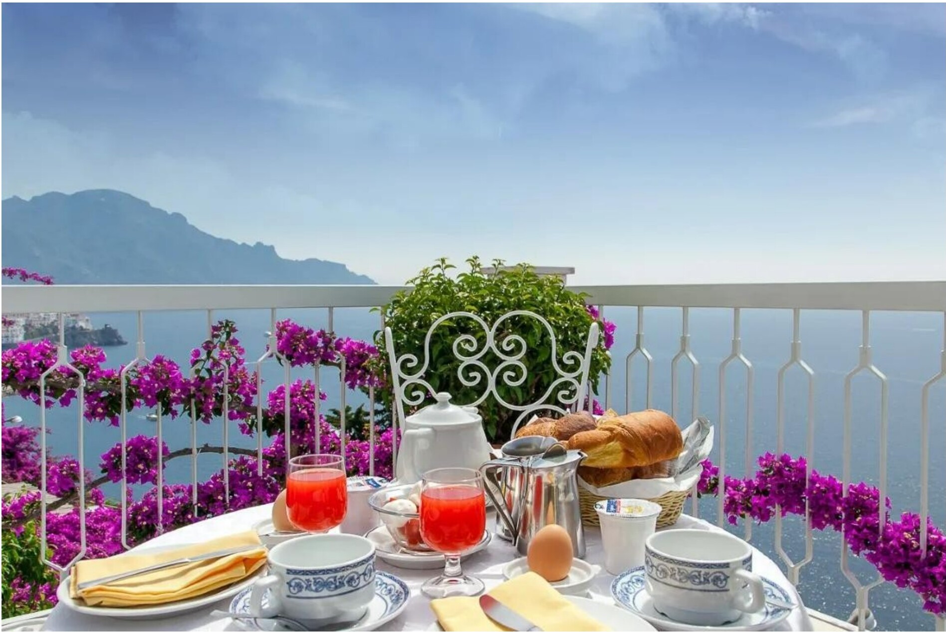 A breakfast table on a balcony overlooking the sea.