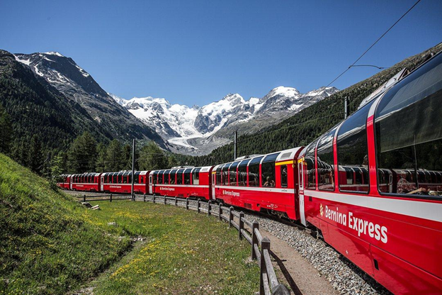 The red Bernina Express train winding through an Alpine valley with snow-capped peaks.