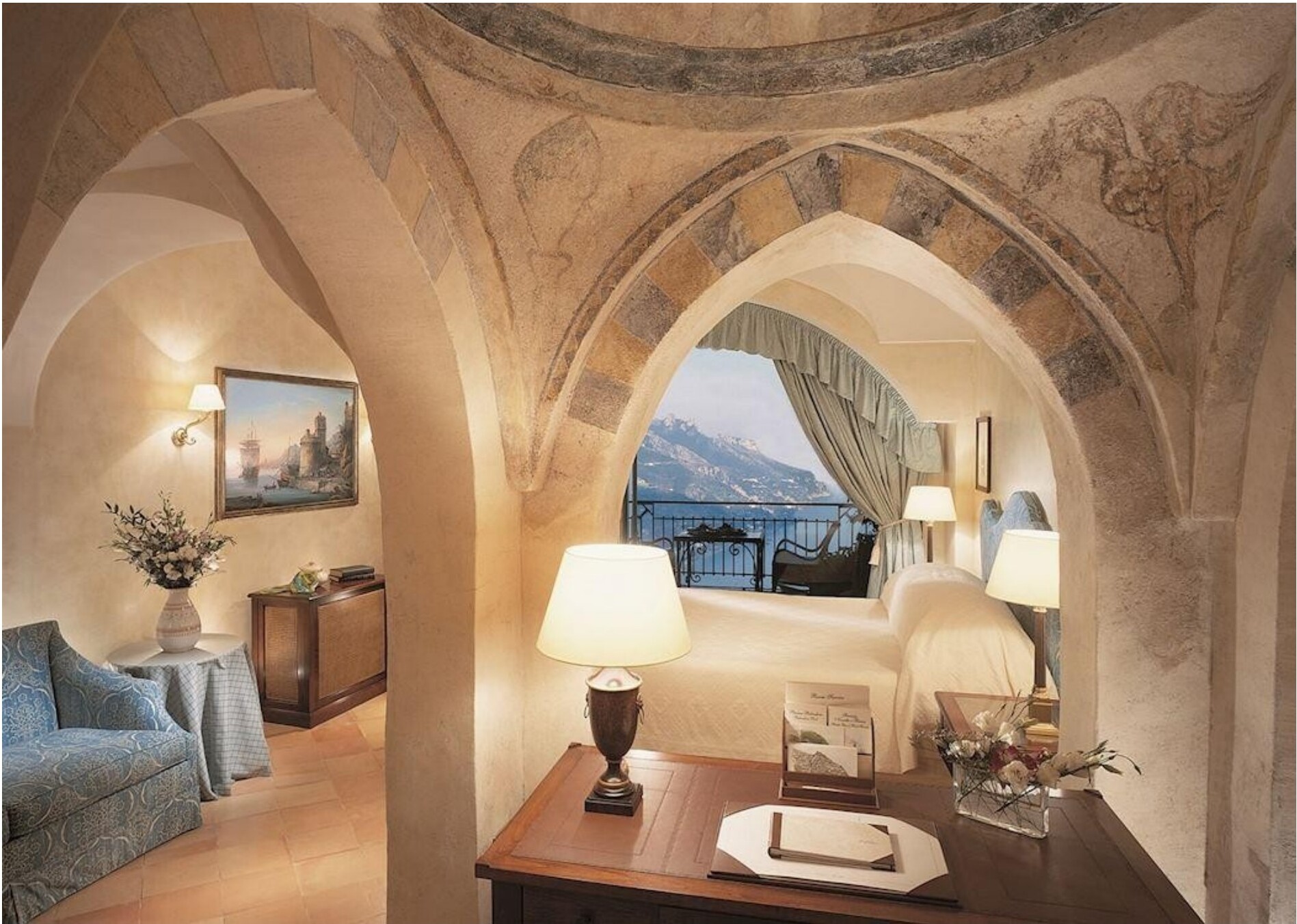 A stone-arched suite at Caruso with a sea-view balcony and blue sofa sitting area