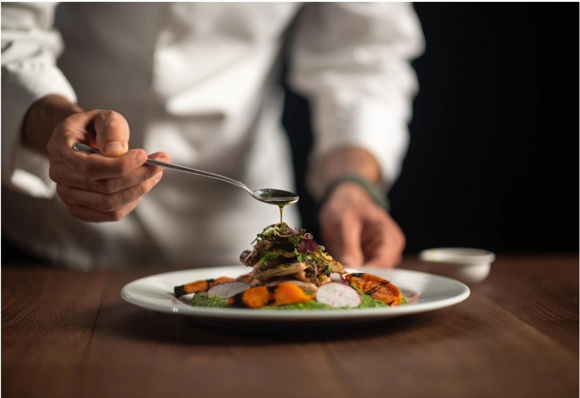 A chef carefully drizzling sauce over a plated dish.
