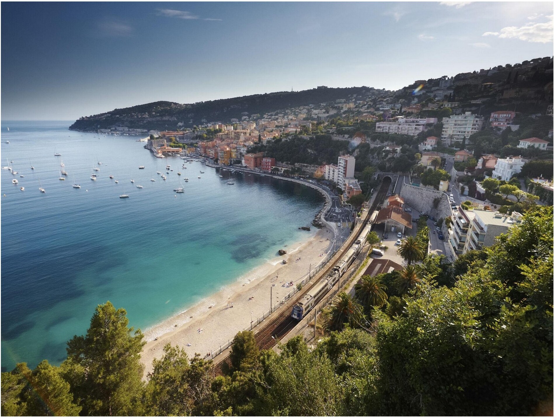 A coastal Italian town with turquoise water and a train traveling along the shoreline
