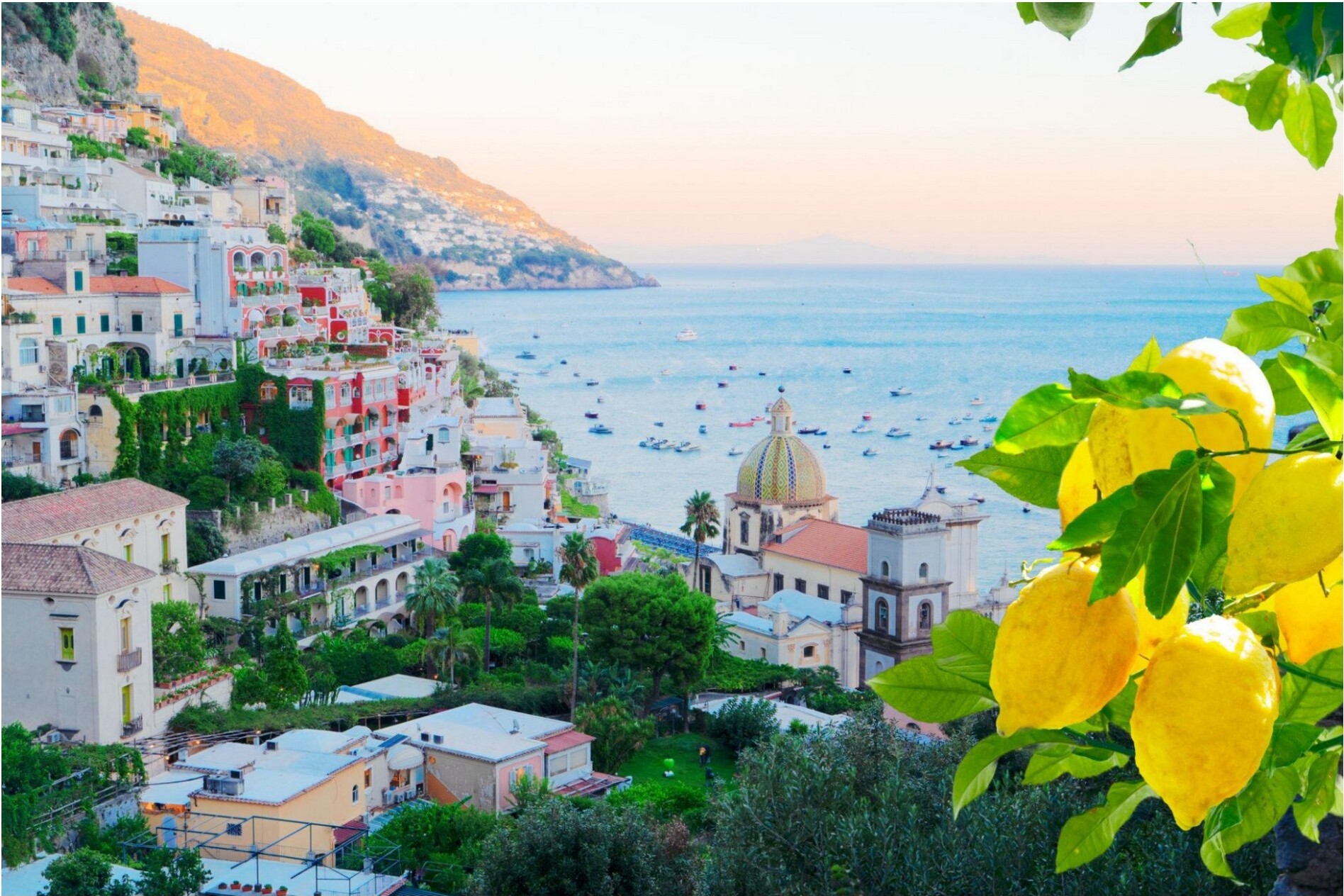 A coastal town with colorful buildings on a hillside overlooking the sea, with lemons in the foreground.