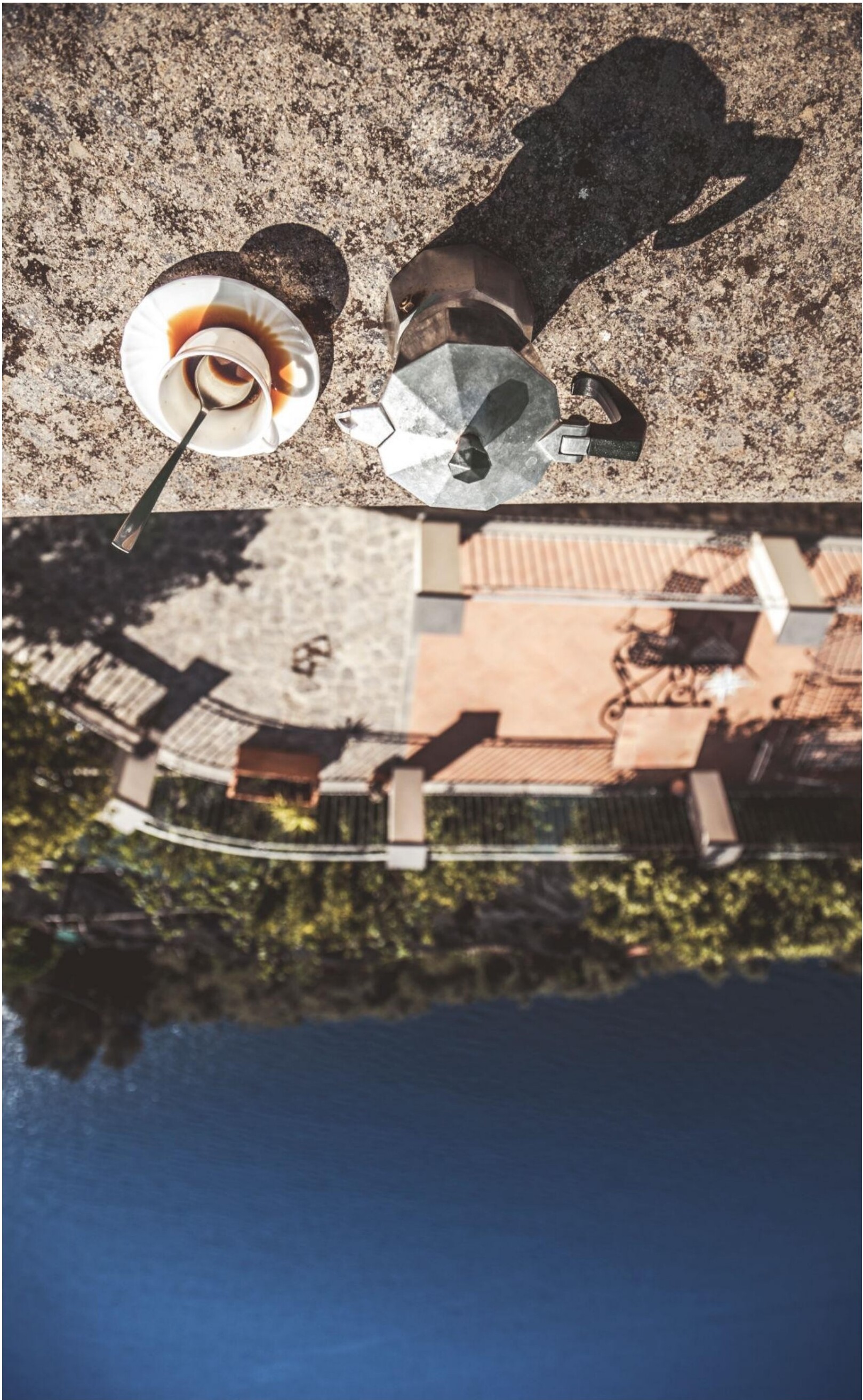 A cup of coffee and a moka pot on a stone surface.