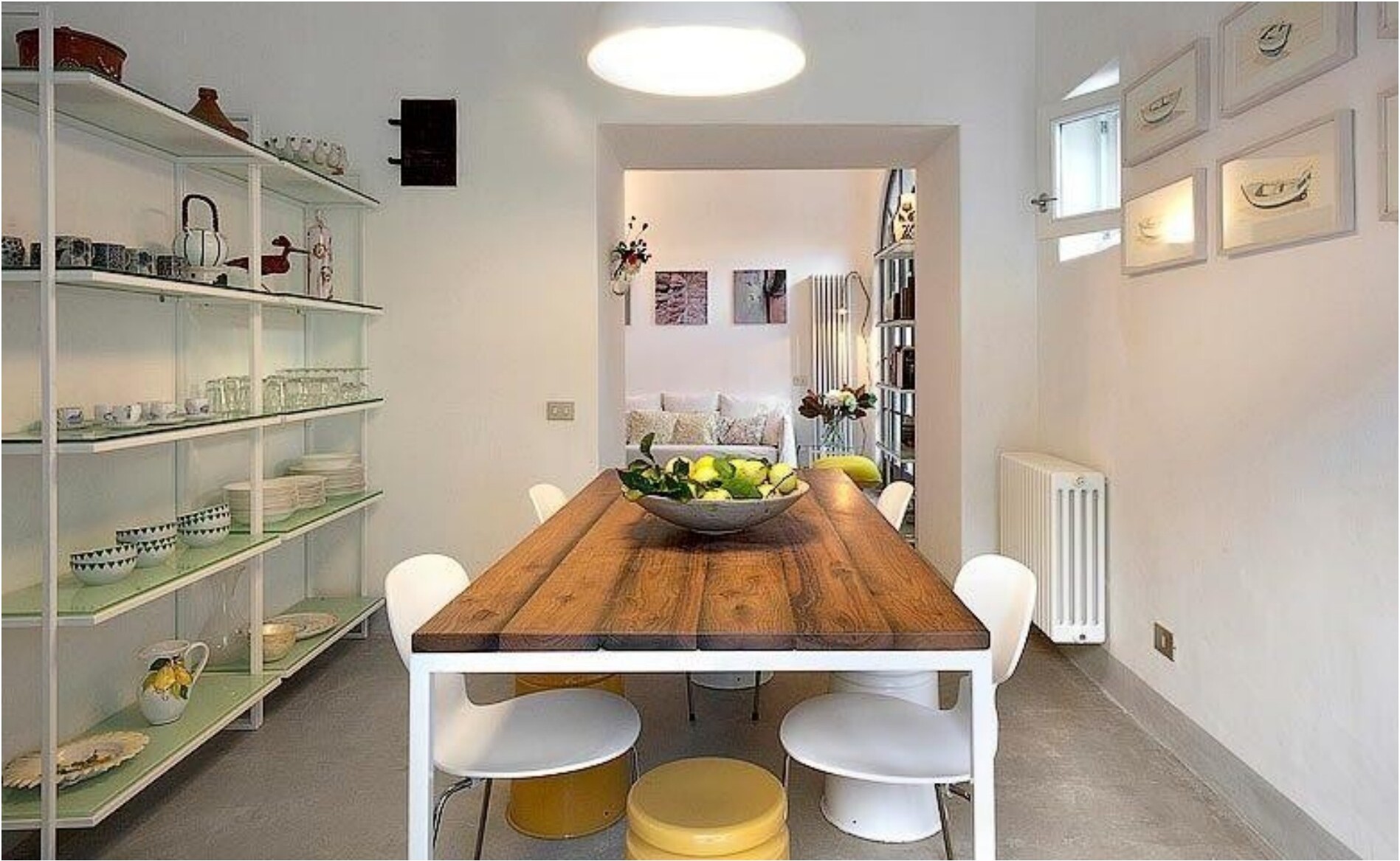 A dining area with a wooden table, white chairs, and shelves filled with dishes.