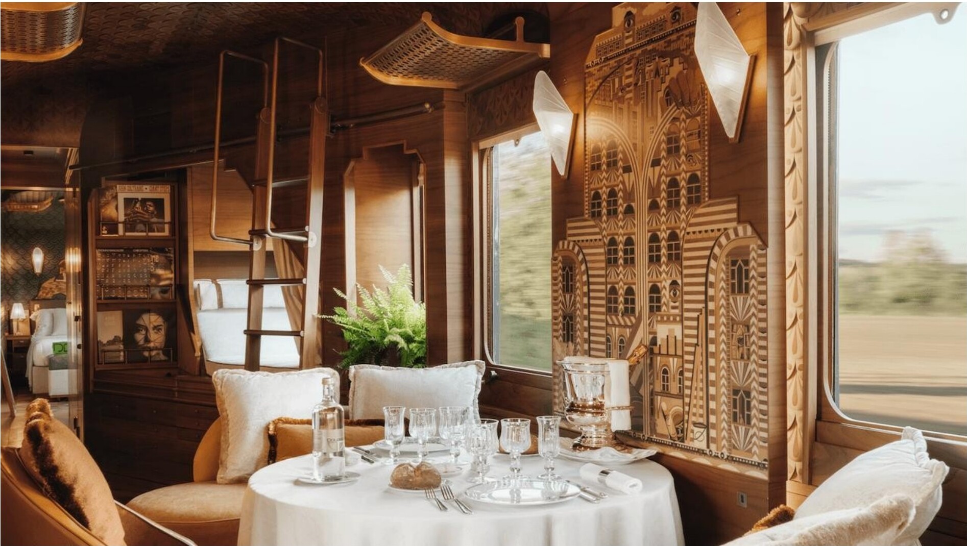 A dining table set for two inside a wood-paneled carriage with passing countryside