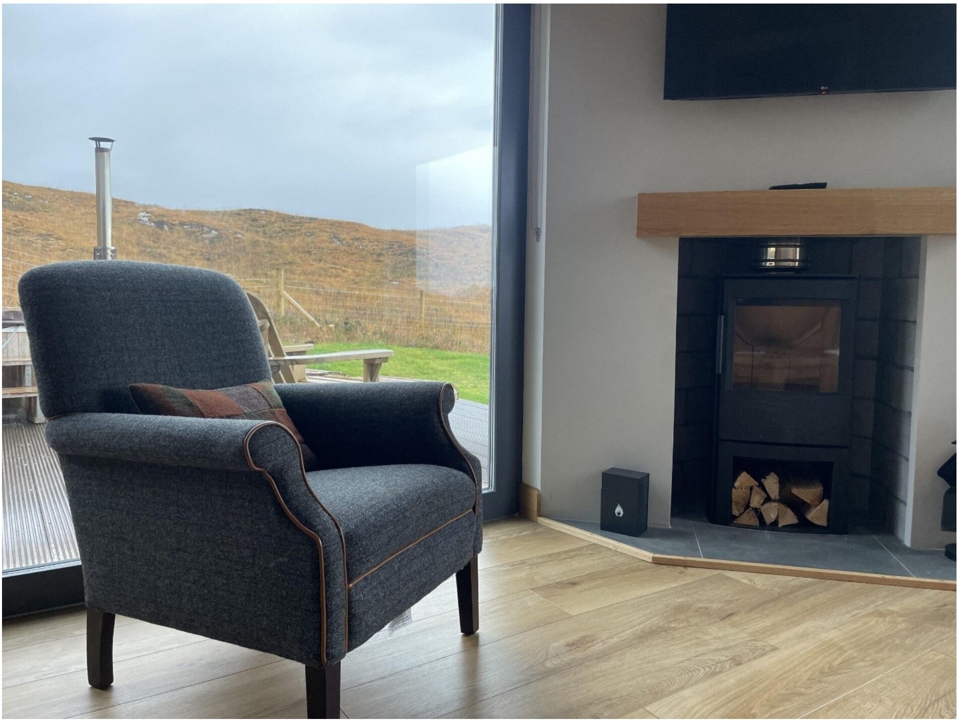 A wood-paneled drawing room with armchair, fireplace, and a window onto the Highland landscape