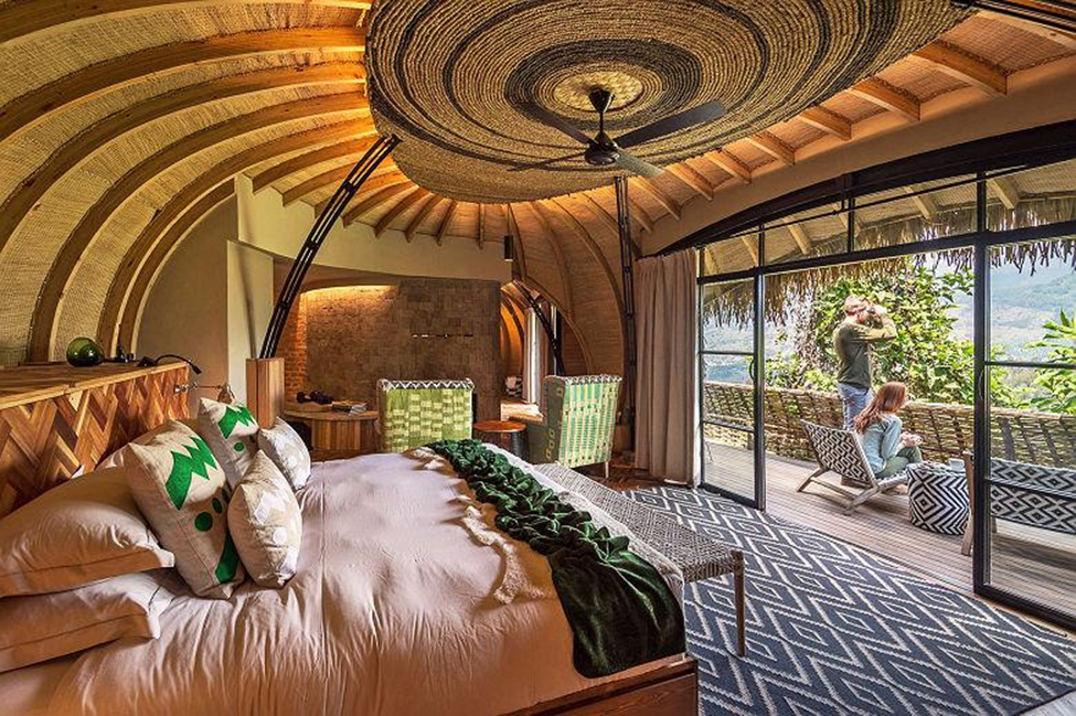 Interior of a thatched luxury suite with woven ceiling, fireplace and views to the forested hills