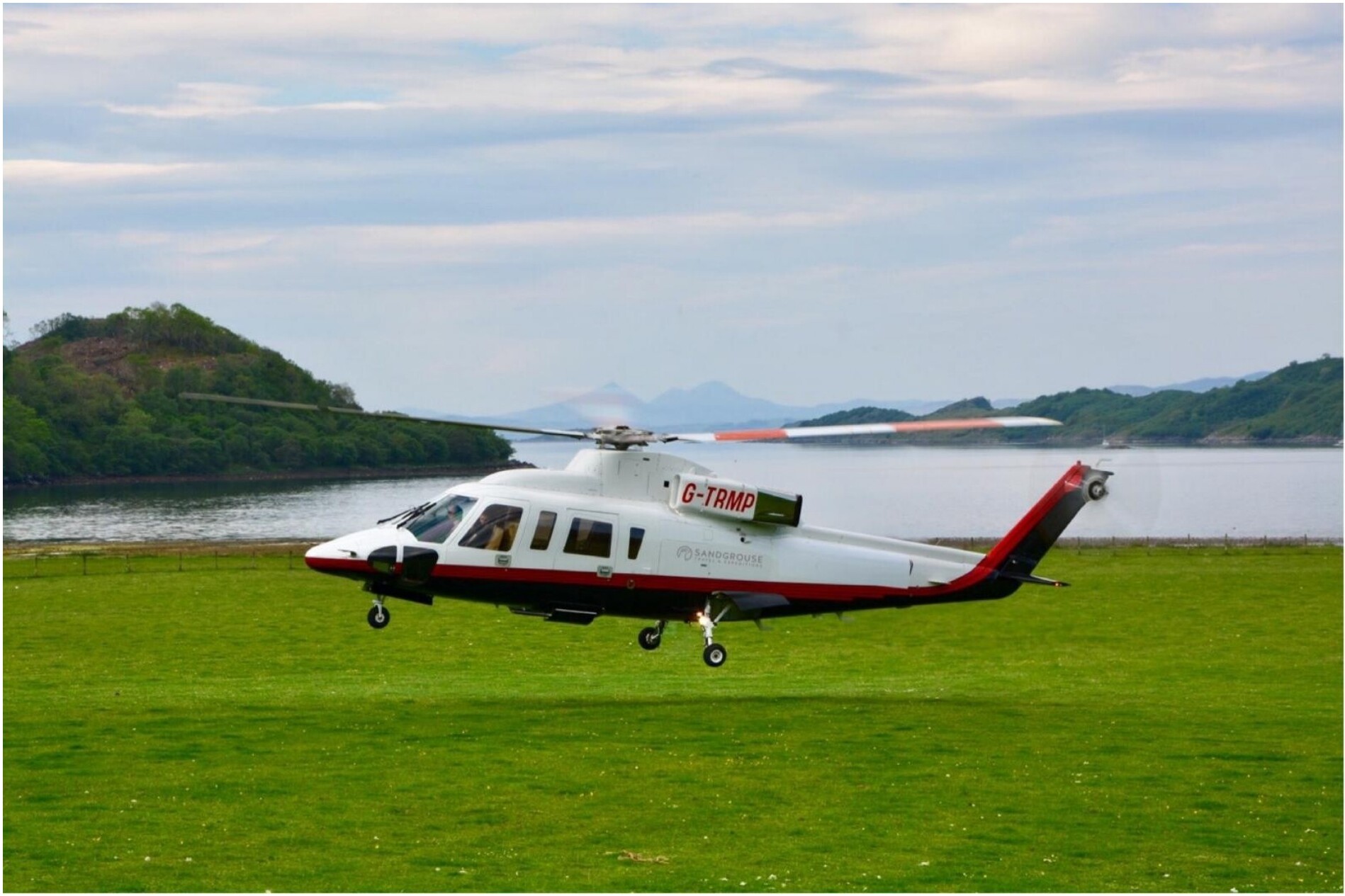 A private helicopter resting on a grassy field beside a Highland loch