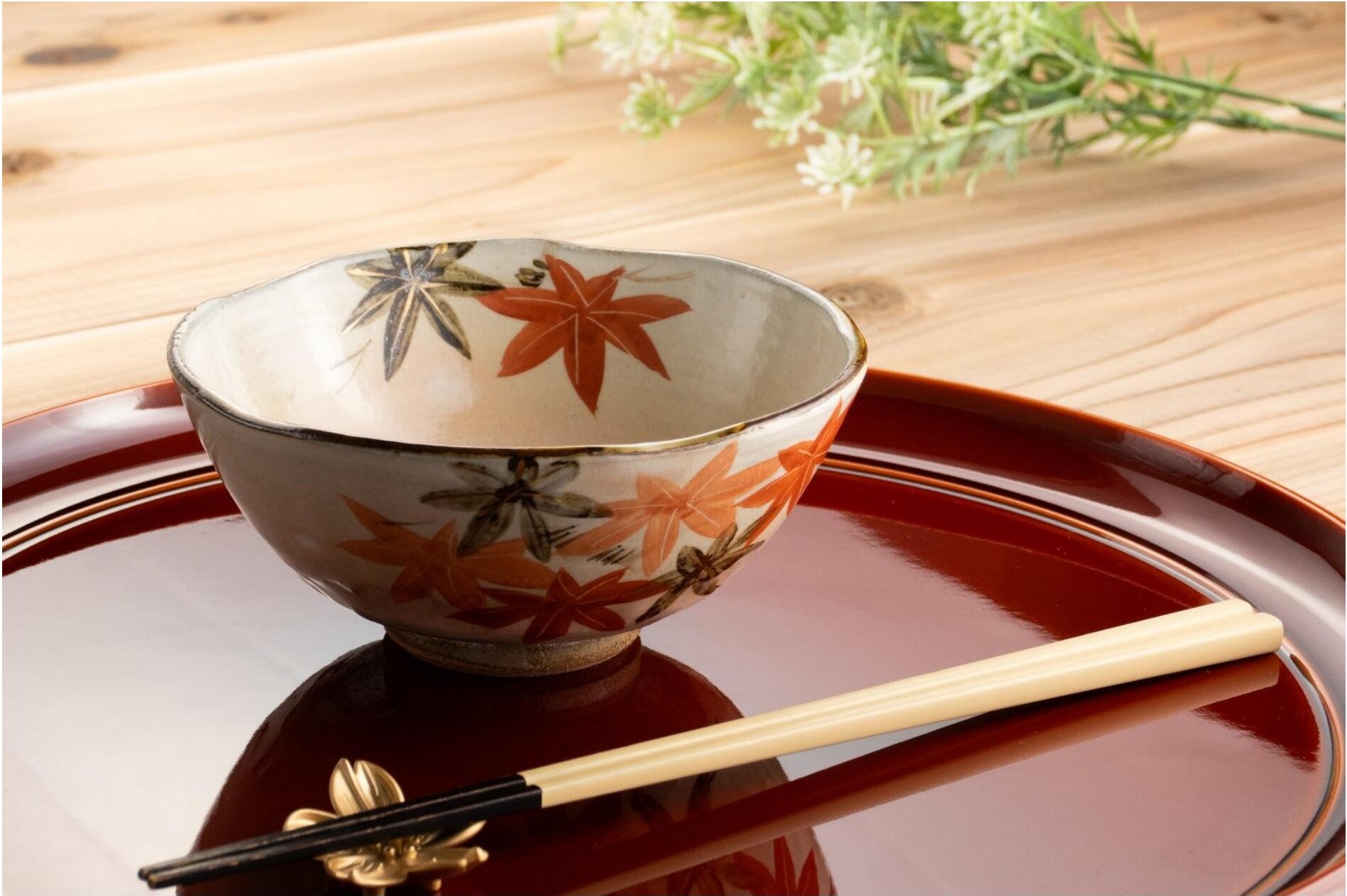 A Japanese ceramic bowl with maple-leaf motifs and chopsticks on a wooden table.
