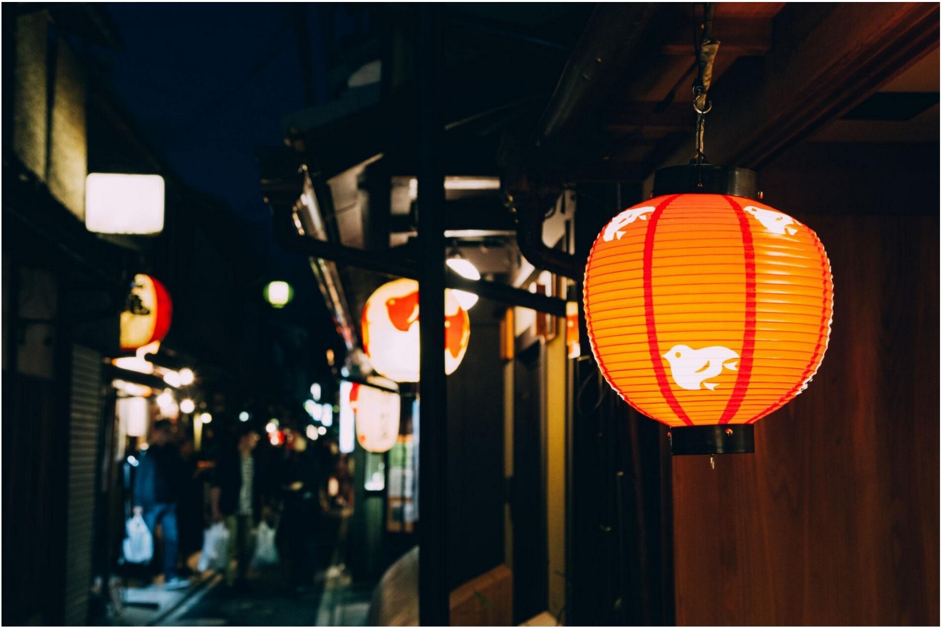 A narrow Kyoto alleyway at night lit by glowing red paper lanterns.