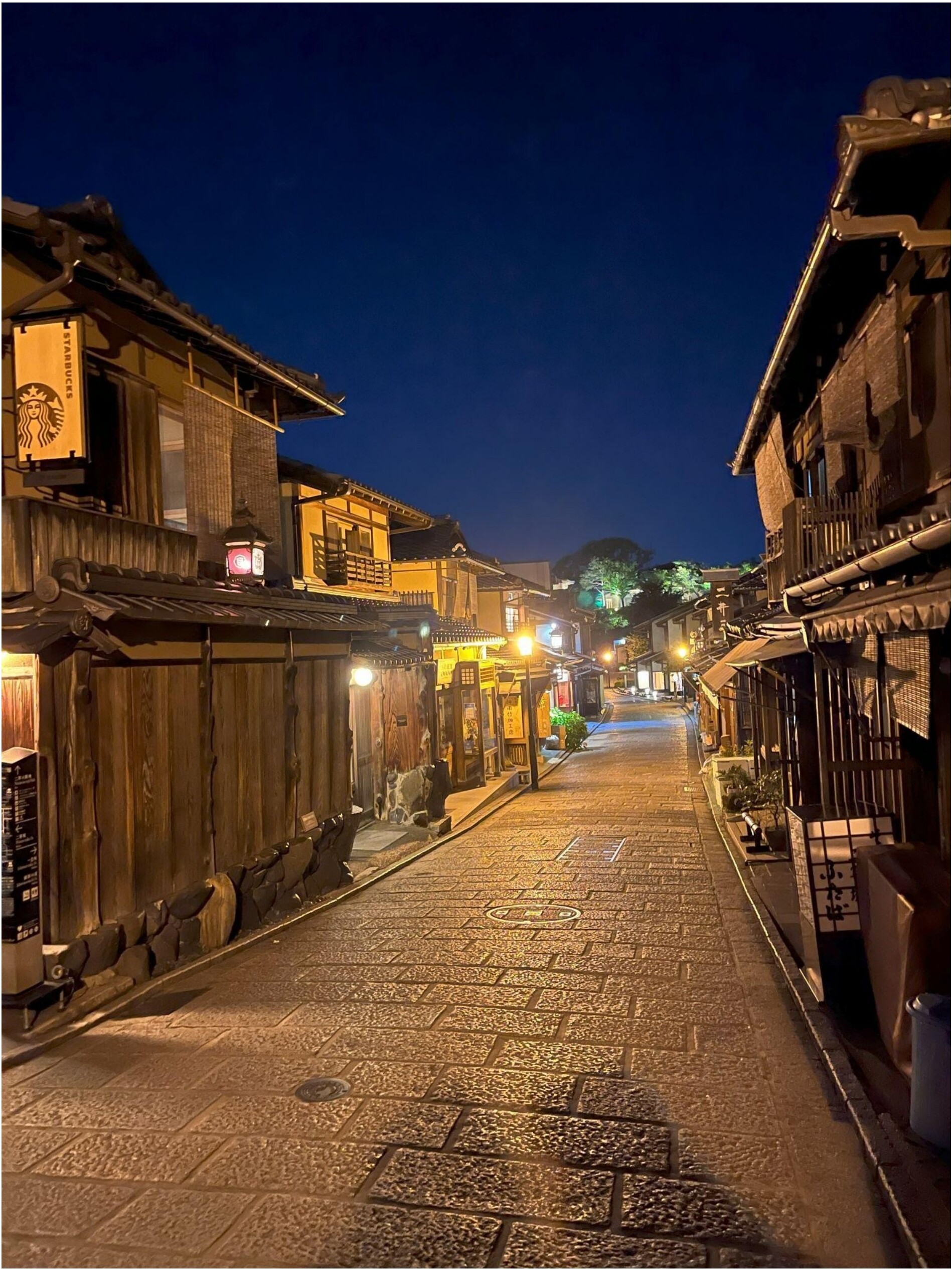 A traditional Gion street at night with wooden buildings and glowing lanterns.
