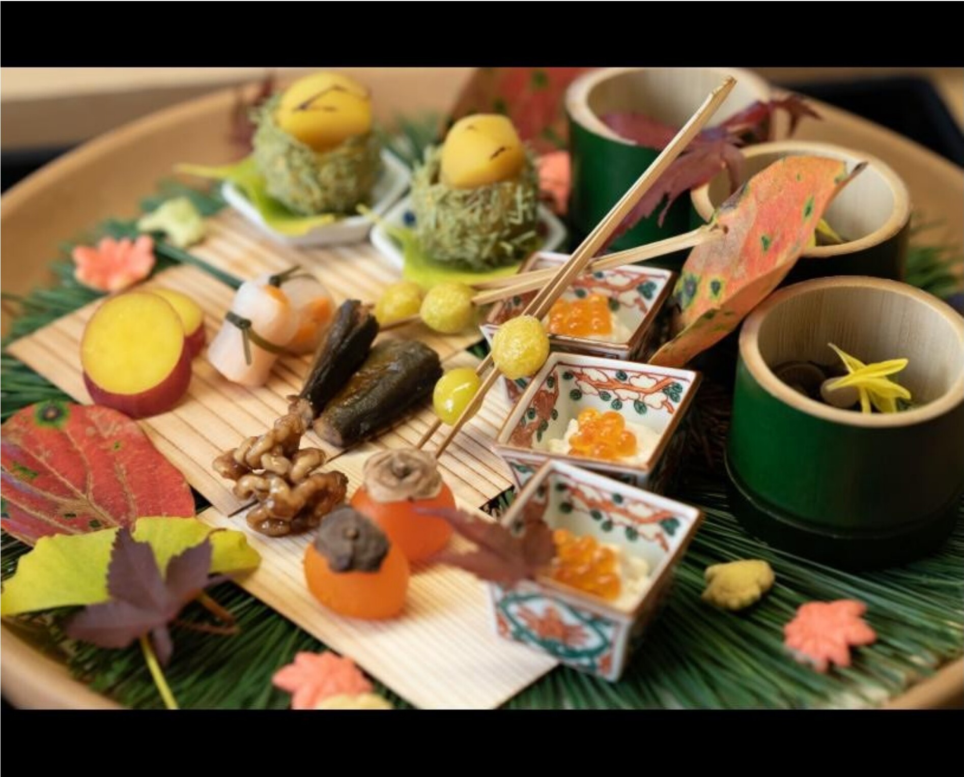 An autumn kaiseki dinner with persimmons, walnuts and small seasonal dishes presented on a bamboo mat with maple leaves.