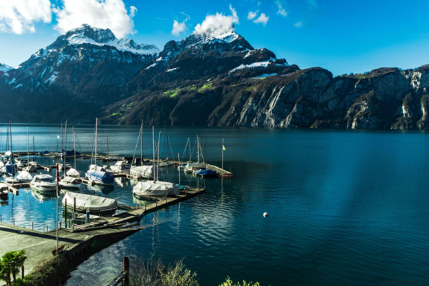 A serene Swiss alpine lake with sailboats moored at a marina beneath snow-dusted peaks.