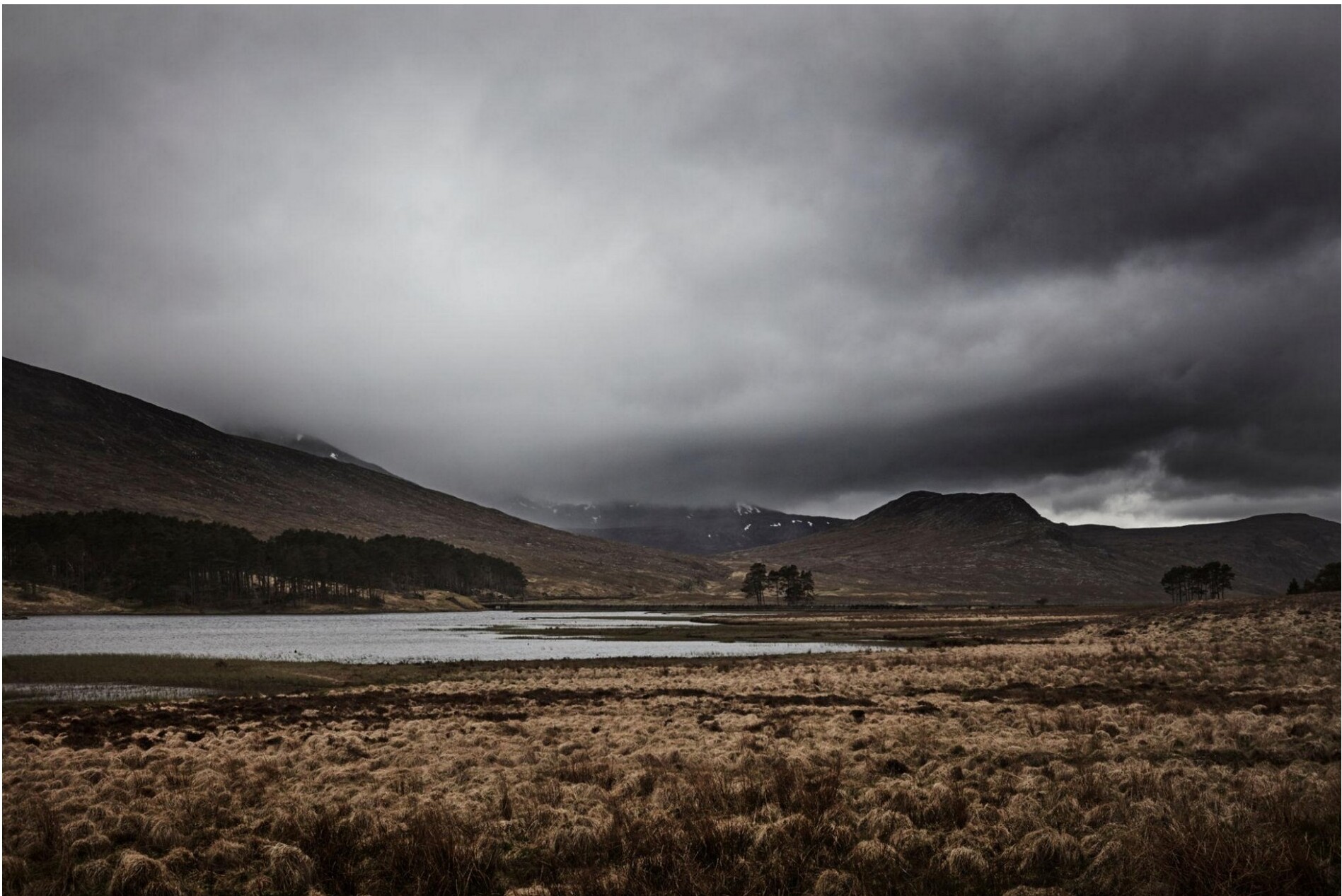 A Highland lake set beneath dark clouds and distant mountains