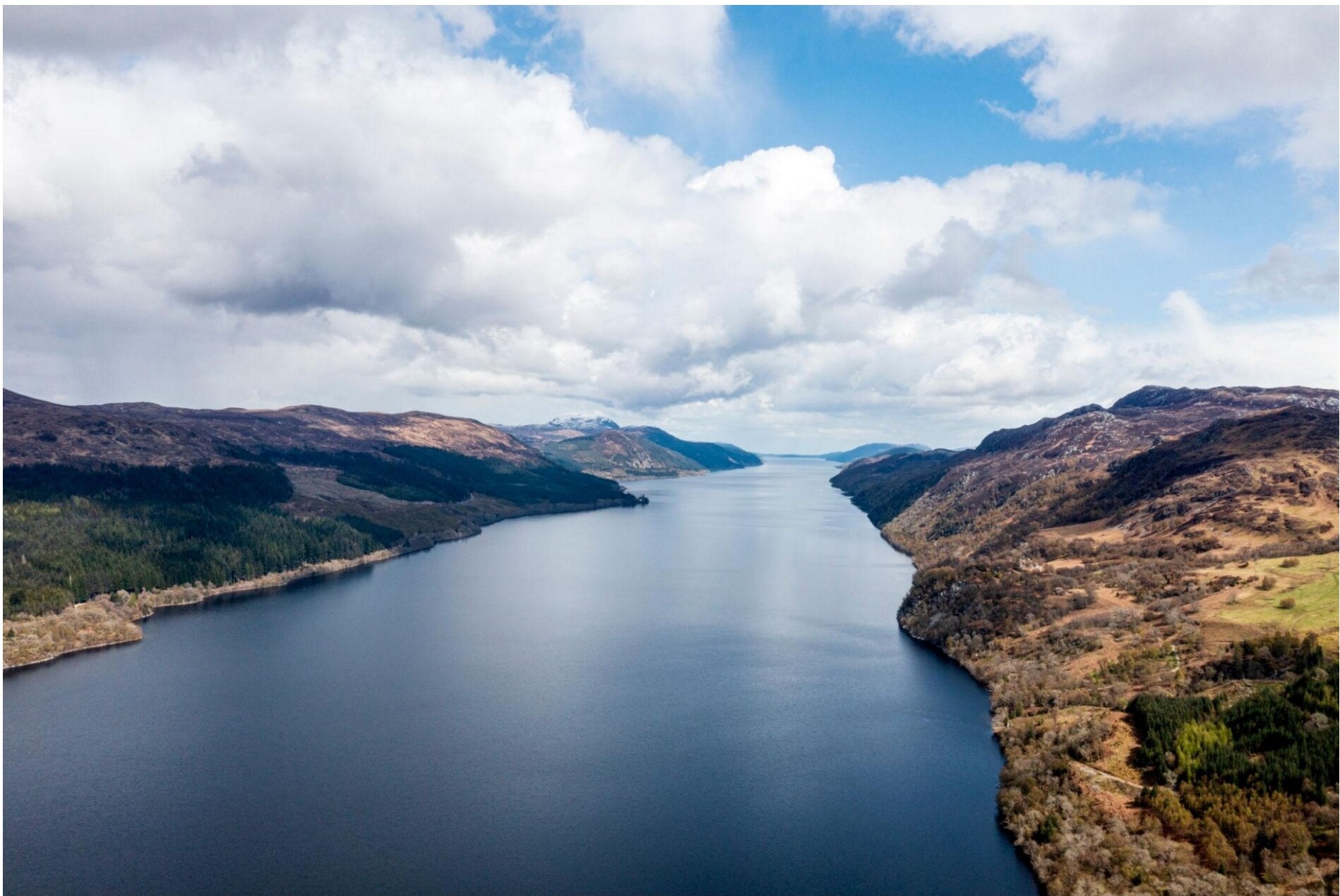 Aerial view of a long narrow loch surrounded by Highland forests