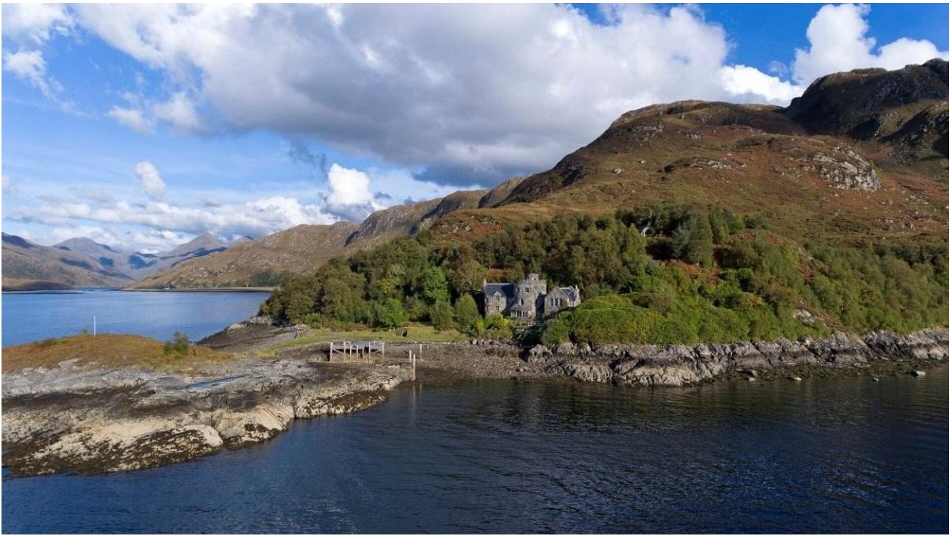 A Highland house perched beside a still loch under a cloudy sky
