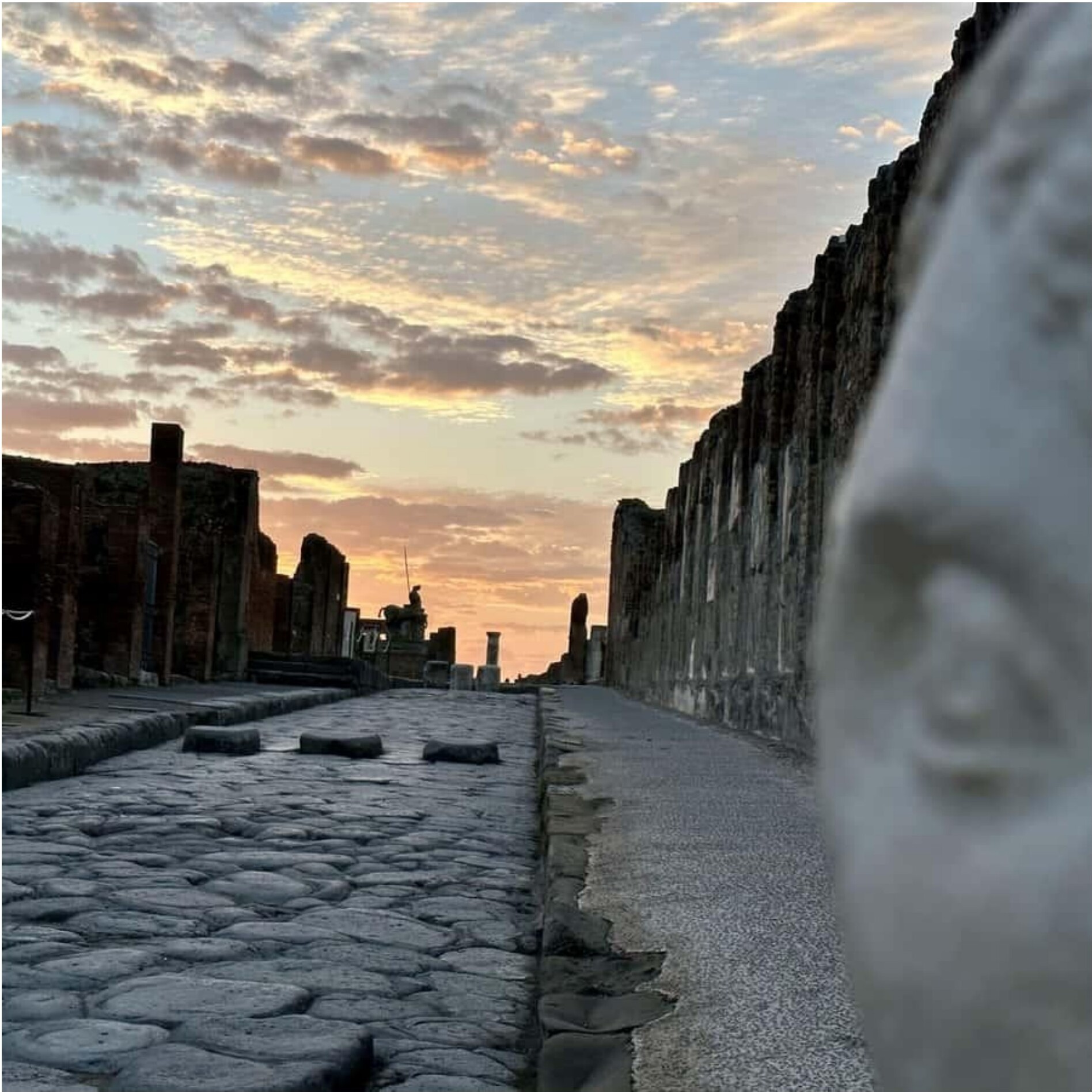 Stone-paved street of Pompeii at sunset with a statue in the foreground