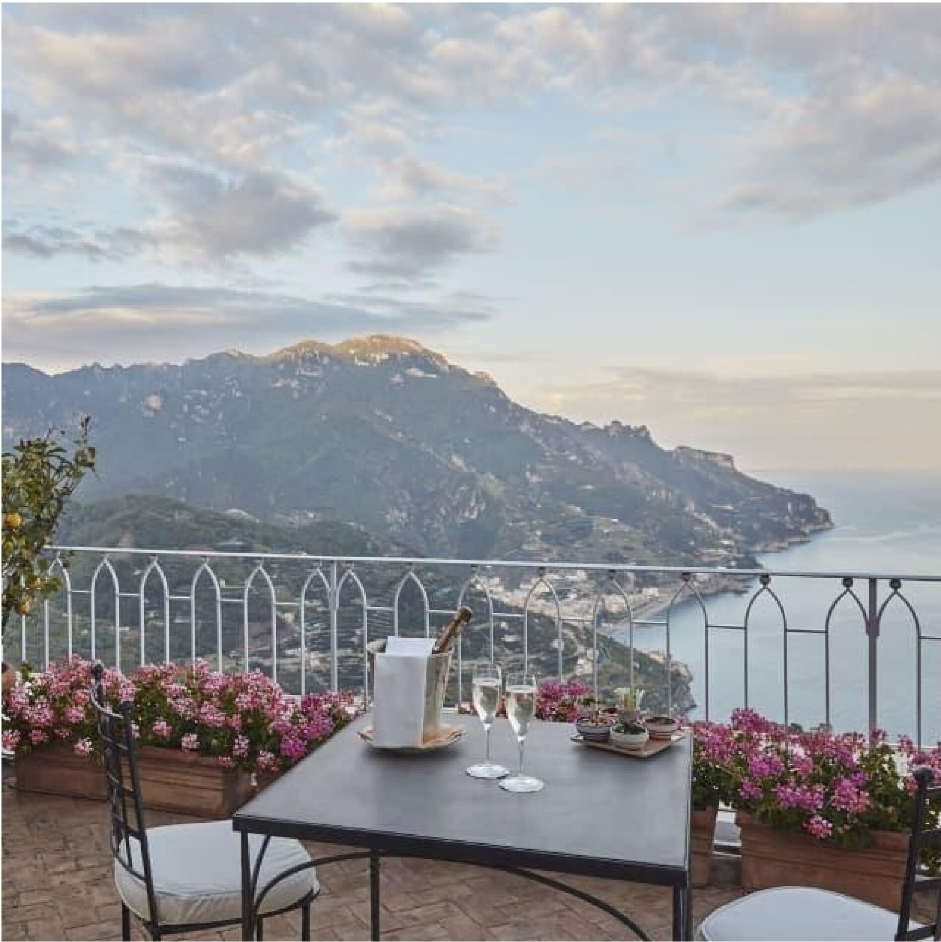 A terrace overlooking the Amalfi Coast with champagne, flowers, and the sea