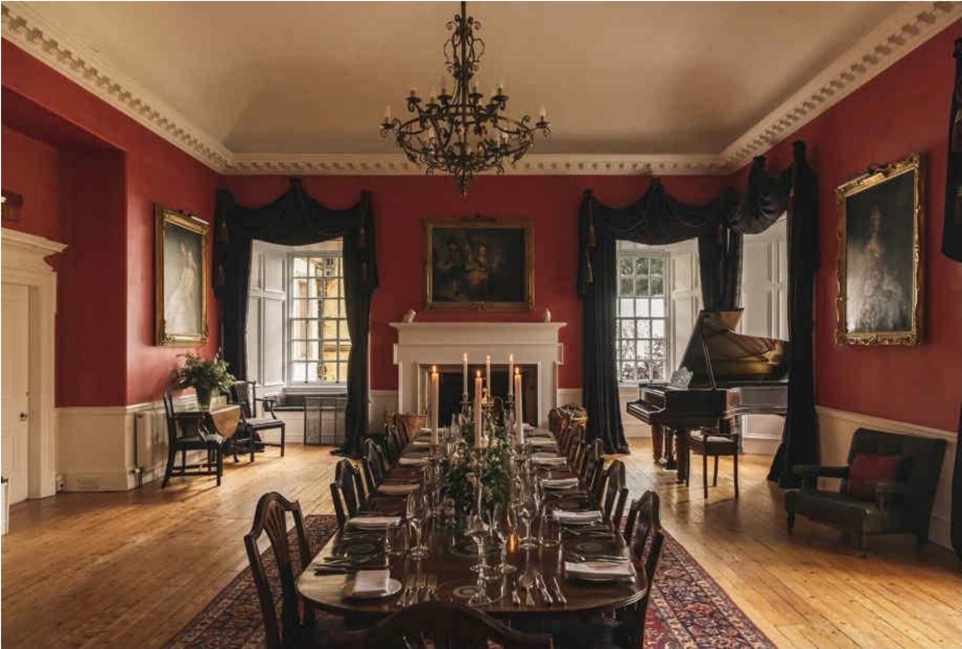A grand red-walled dining room with a long candle-lit table and chandelier