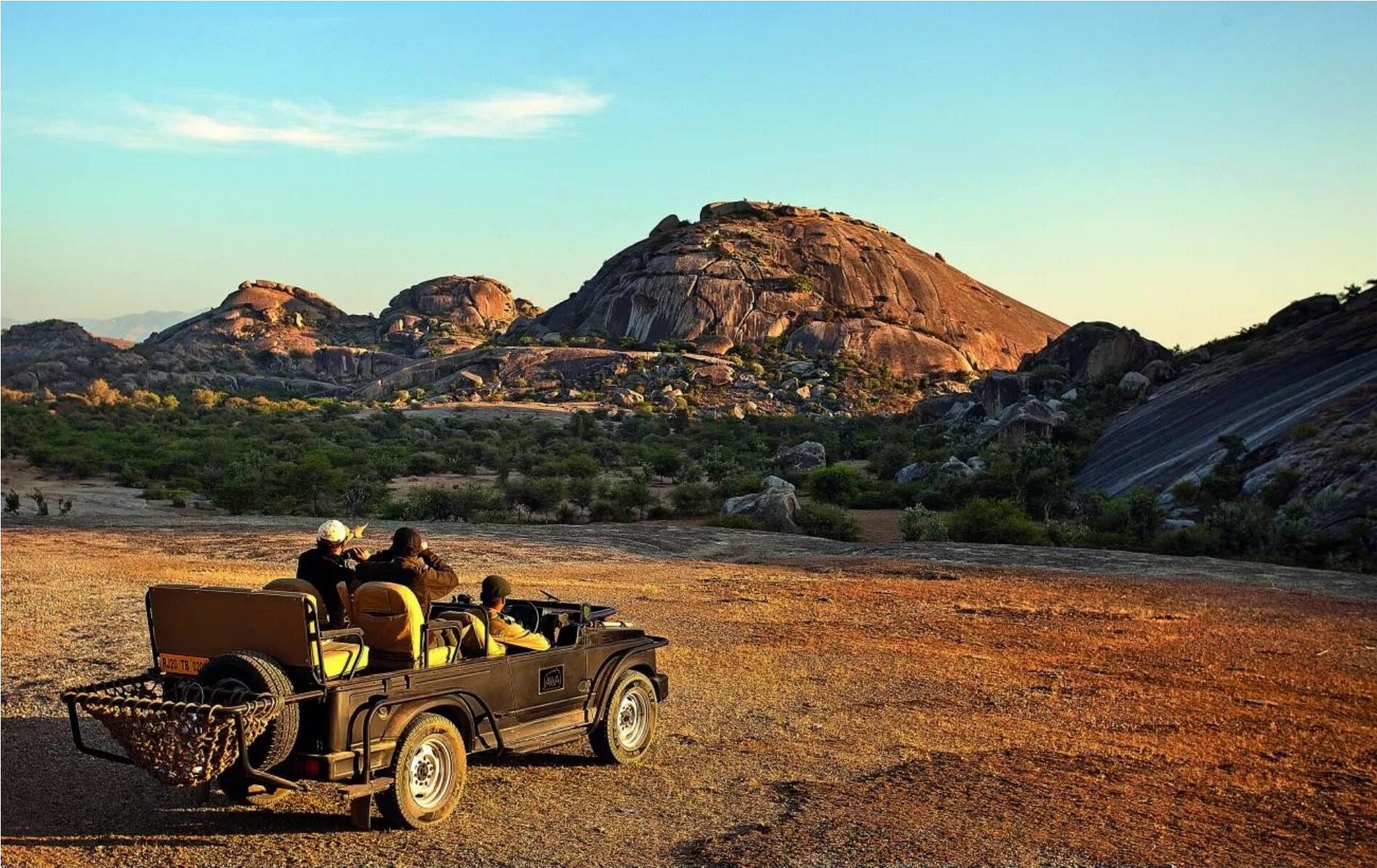 A safari vehicle driving through a rocky landscape at golden hour.