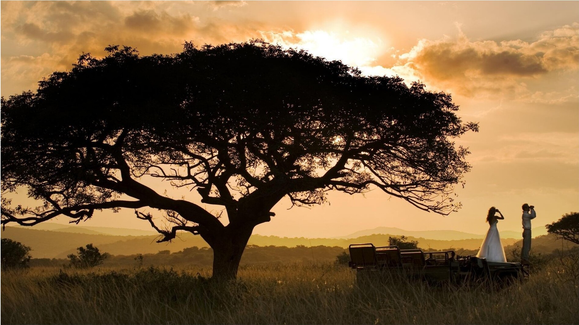 Silhouetted travelers near a safari vehicle at sunset