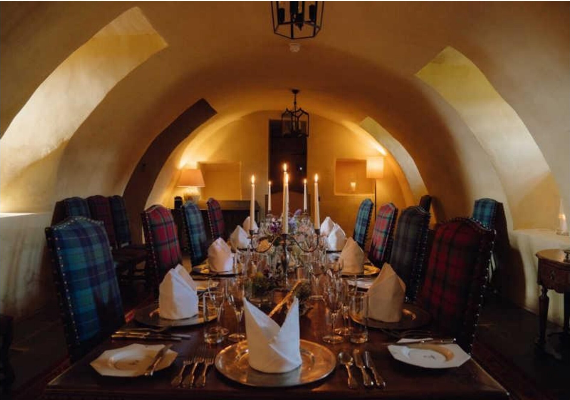 A long dining table set in a vaulted hall with tartan-upholstered chairs