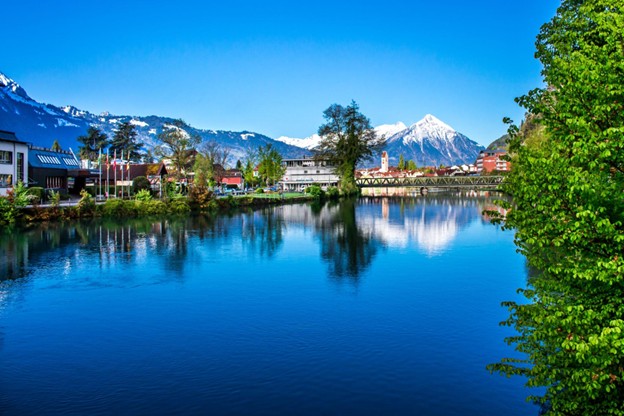 A Swiss lakeside town with snow-capped mountains reflected in calm blue water.