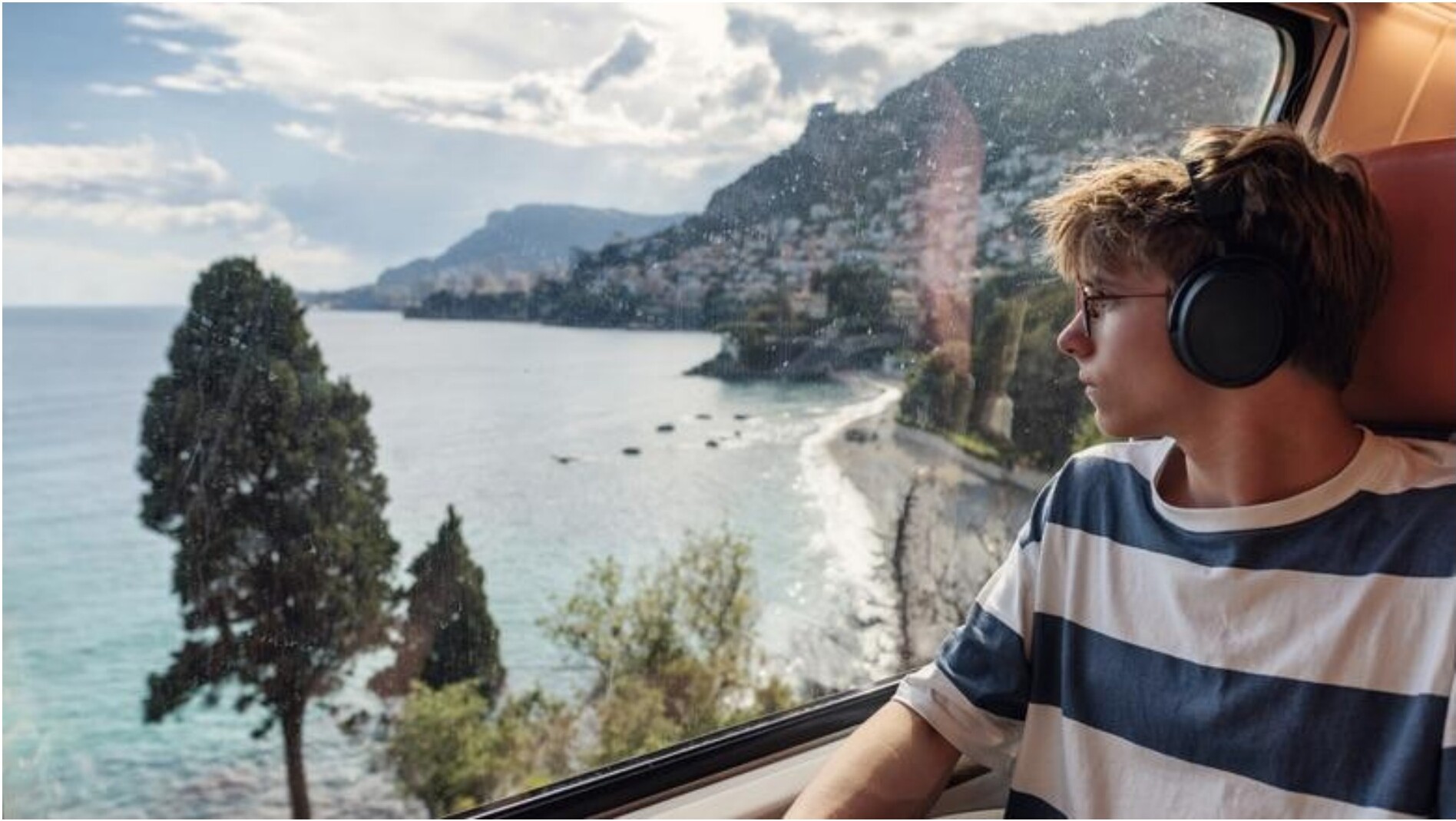 A passenger looking out a train window at coastal mountains and sea