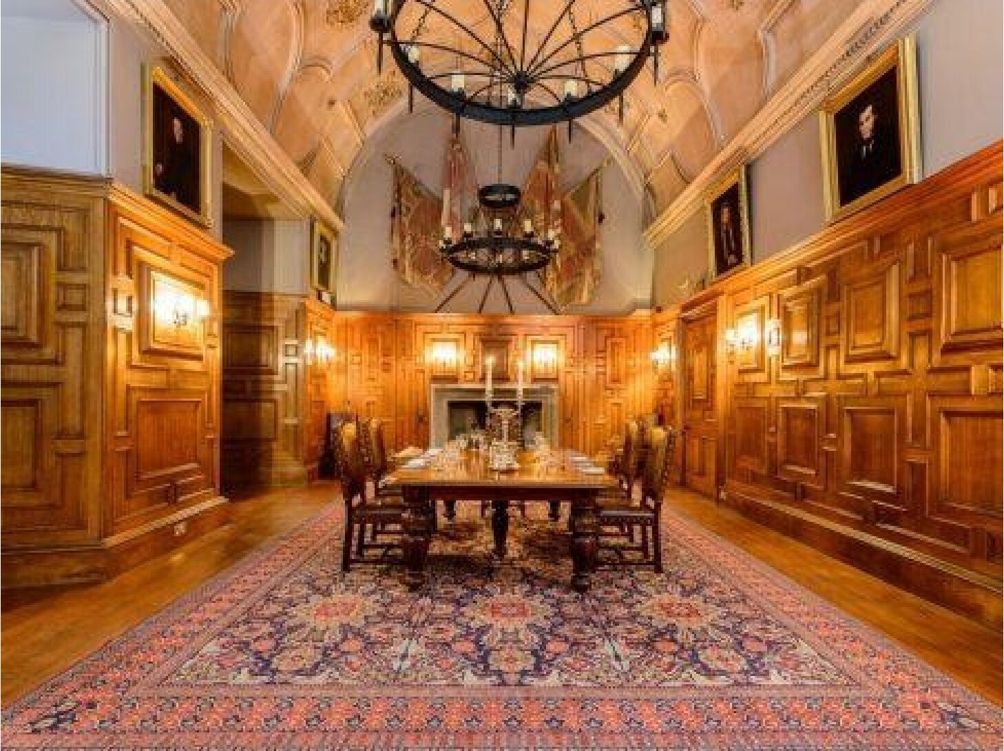 A wood-paneled hall with vaulted ceiling, large rug, and ancestral portraits